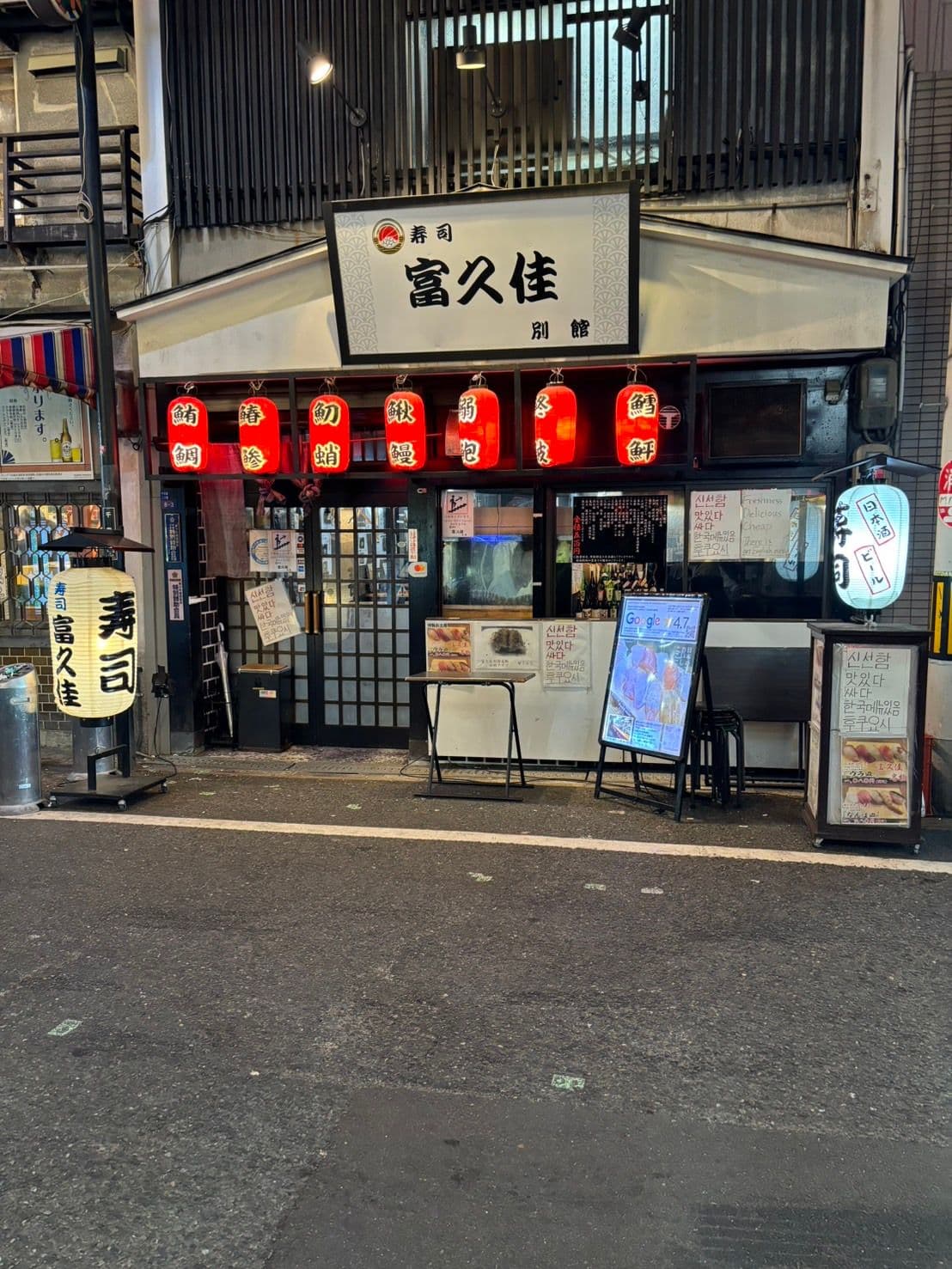 夜の富久佳 別館の外観。「寿司 富久佳 別館」の看板と、魚の名を記した赤提灯が並ぶ店頭