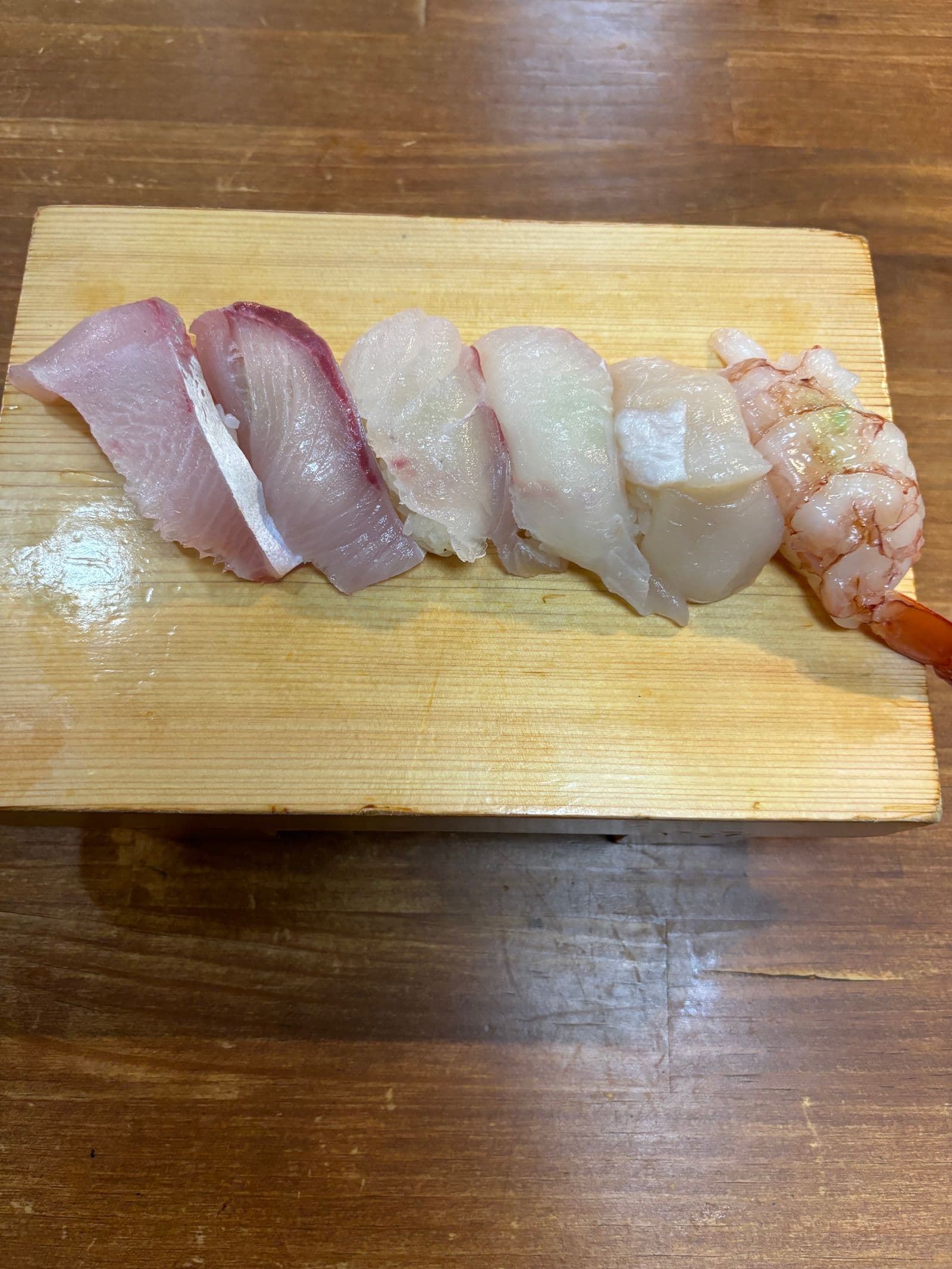 木のつけ台に並ぶにぎり寿司五貫。海老、帆立、白身、はまち