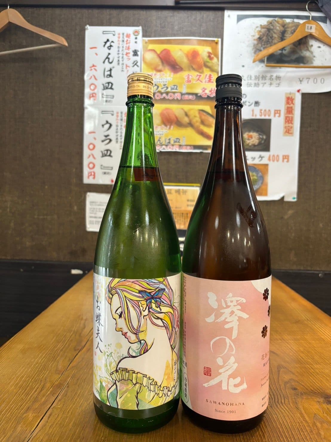 店内のおすすめ品の貼り紙を背景に並べた日本酒の一升瓶二本