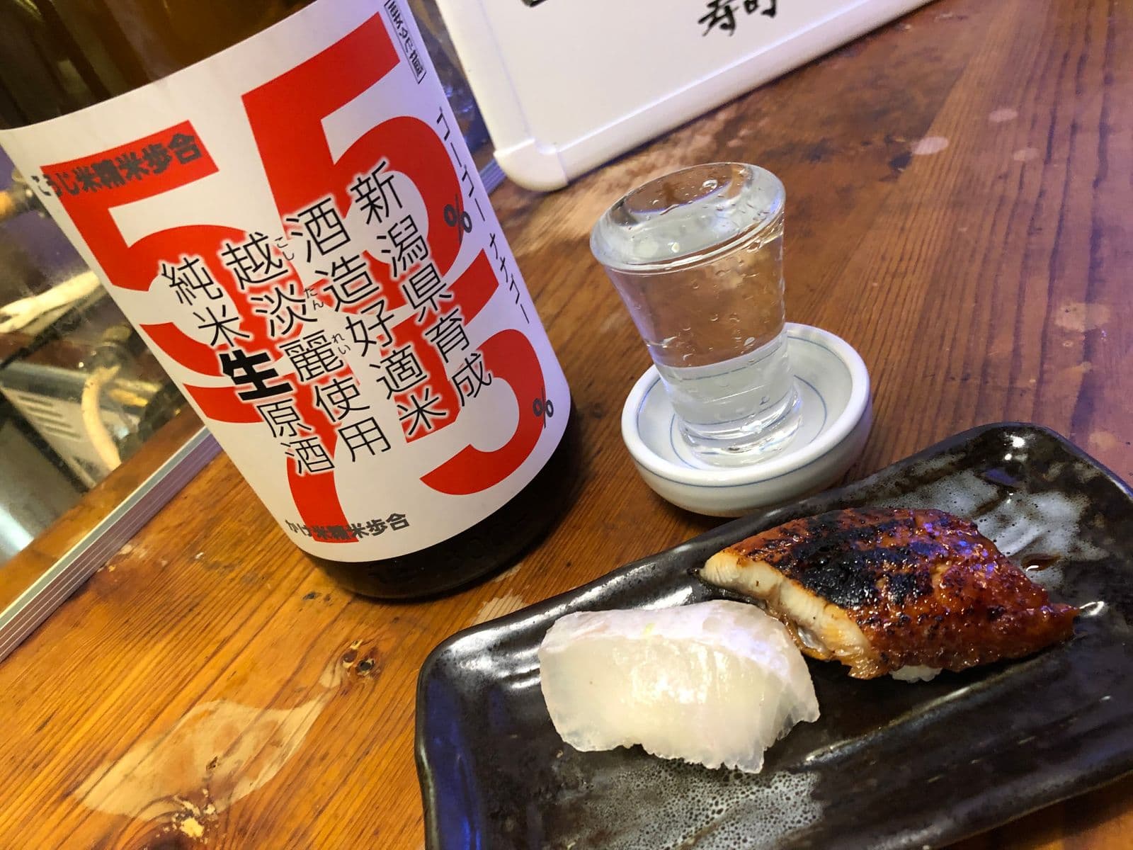純米生原酒の瓶とお猪口、黒い長皿に載せた白身と炙り穴子のにぎり寿司二貫