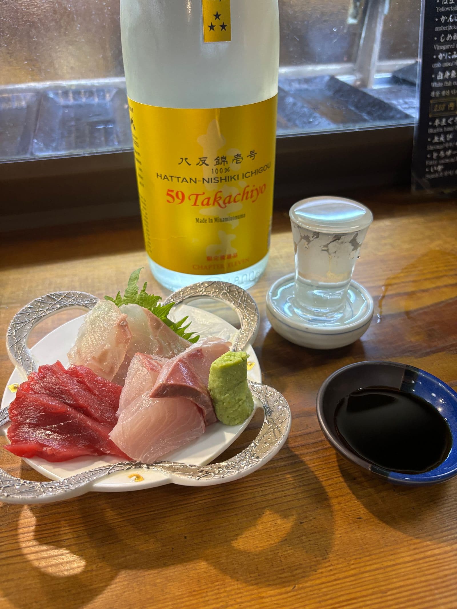 カウンターに置かれた刺身の盛り合わせと日本酒の一升瓶、お猪口、醤油皿